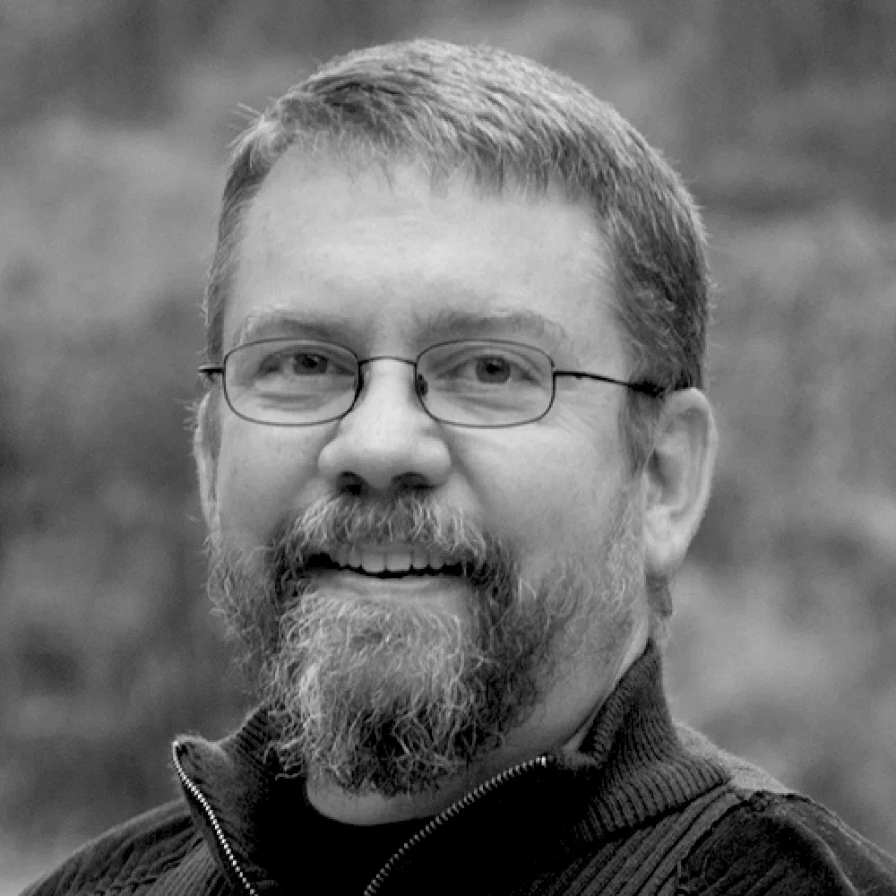 Black-and-white photo of Leonard Smith, an older bearded man with glasses smiling against a softly blurred outdoor background.