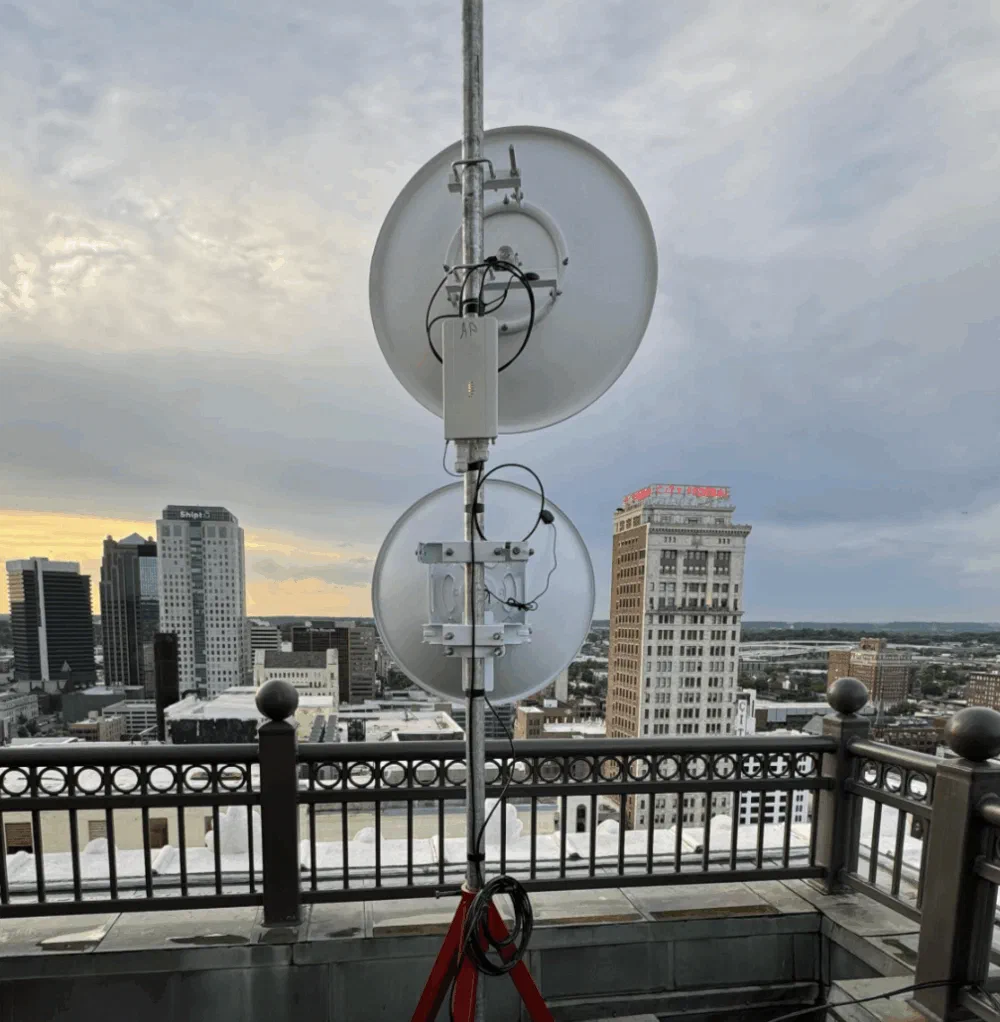 Two stacked parabolic backhaul dishes on a rooftop pole, aimed across the downtown Birmingham skyline under a winter overcast sky.