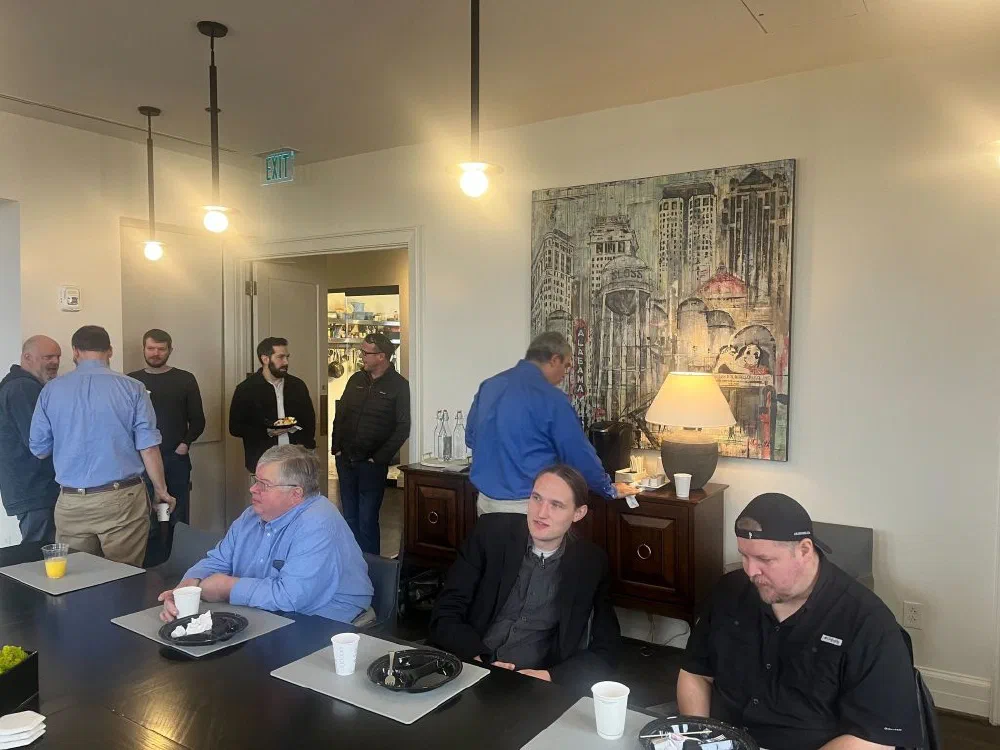 TiDev members mingling at a Birmingham loft brunch, with attendees gathered around a black breakfast table beneath a canvas of an Alabama cityscape.