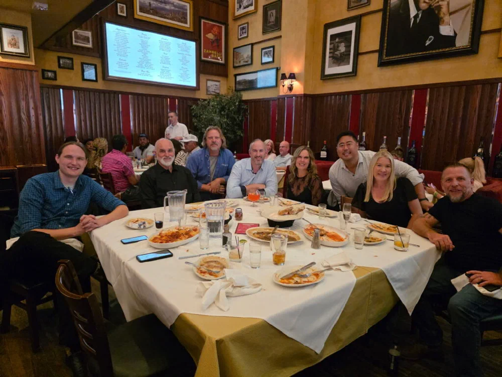 WISPAPALOOZA group dinner photo with nine attendees gathered around a half-eaten Italian-restaurant table, smiling for the camera.