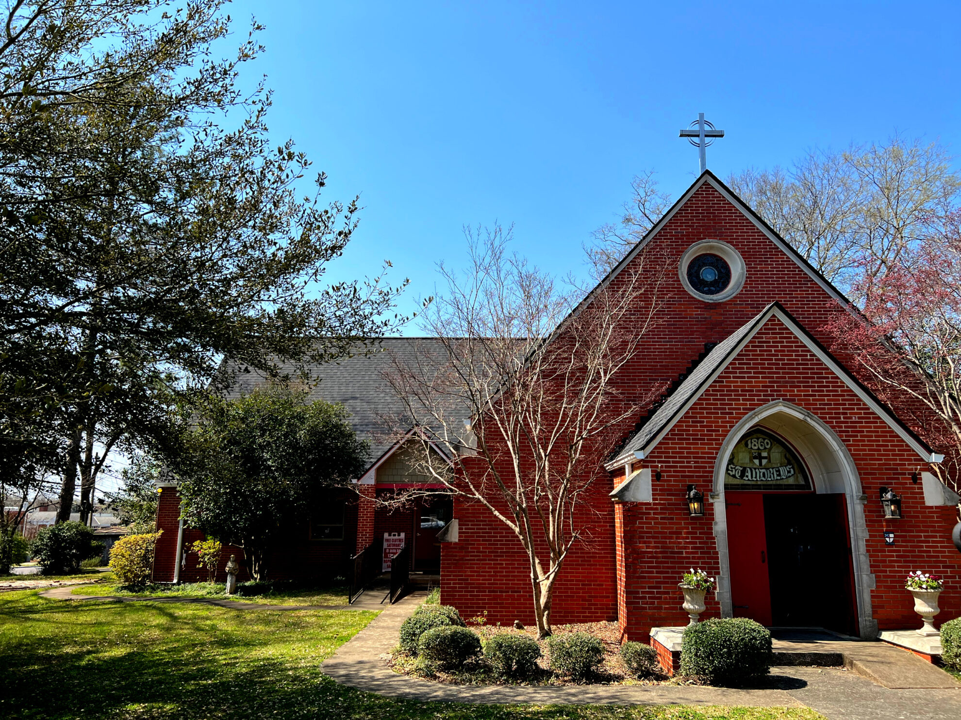Exterior of St. Andrews Episcopal Church in Montevallo, Alabama: a small white-trimmed brick parish with arched doors and a green lawn under a blue sky.